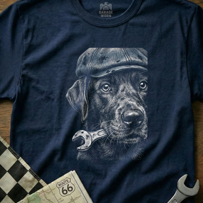 Black Labrador wearing a flat cap holding a wrench in its mouth.