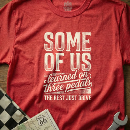 Red t-shirt with "SOME OF US learned on three pedals THE REST JUST DRIVE" text.