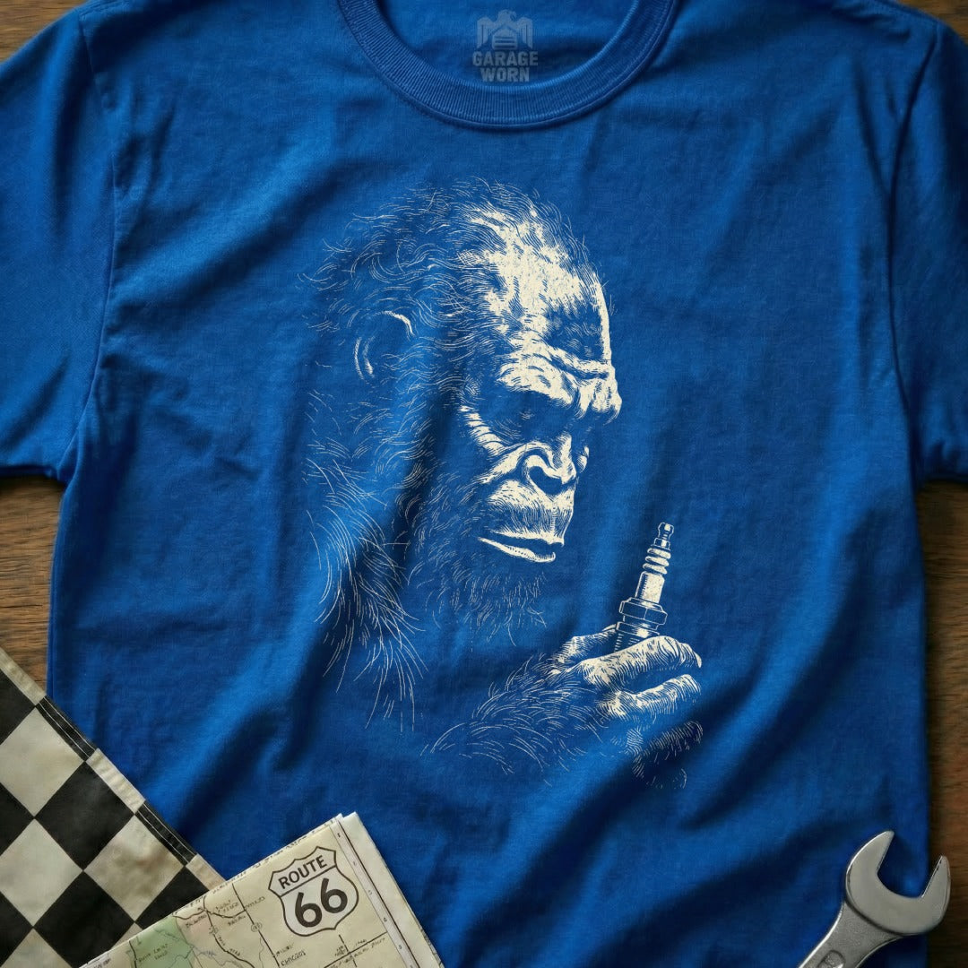 Blue t-shirt with Bigfoot holding a spark plug and a checkered flag.