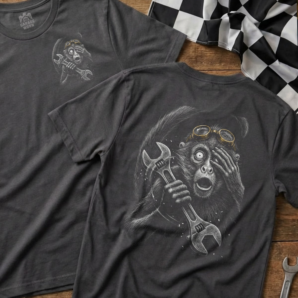 T-shirt with monkey wearing goggles, holding a wrench, on dark grey fabric.