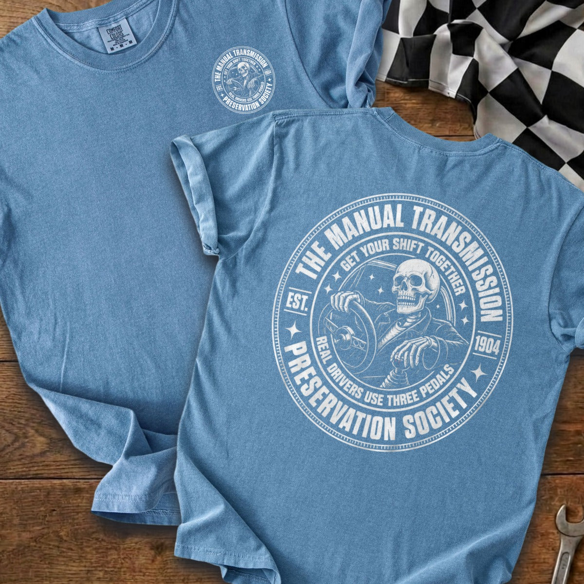 Blue t-shirt with a circular graphic of a skeleton driving, reading "The Manual Transmission Preservation Society."