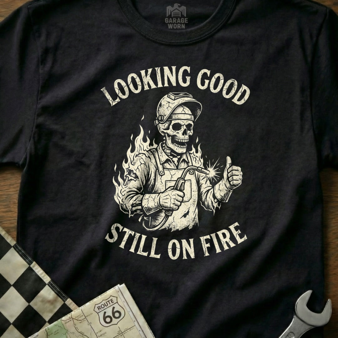Skeleton welder in helmet gives thumbs up with "Looking Good Still On Fire" text.
