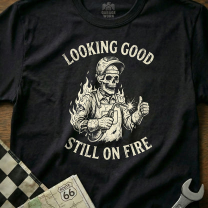 Skeleton welder in helmet gives thumbs up with "Looking Good Still On Fire" text.