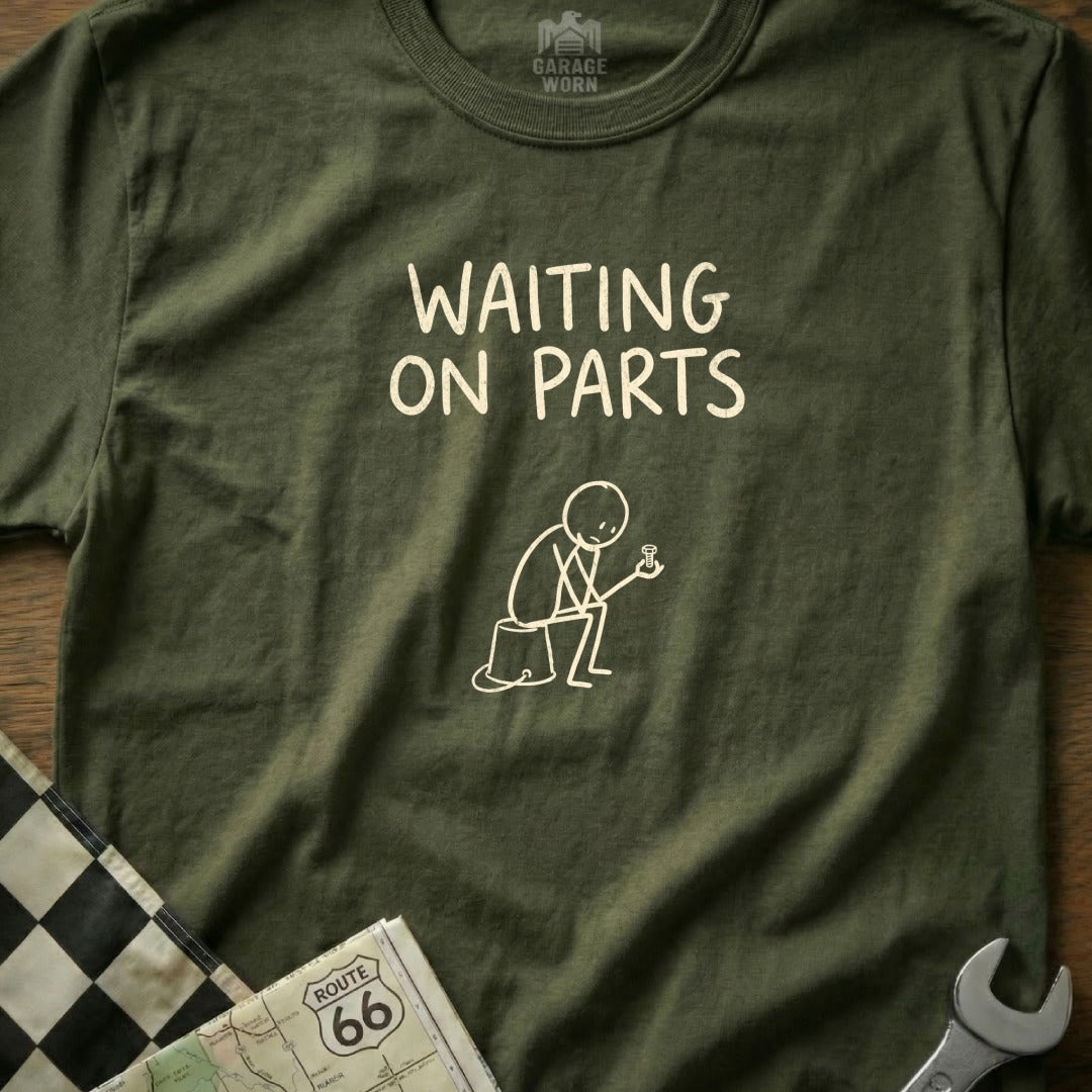 Olive green t-shirt with "WAITING ON PARTS" graphic and stick figure.
