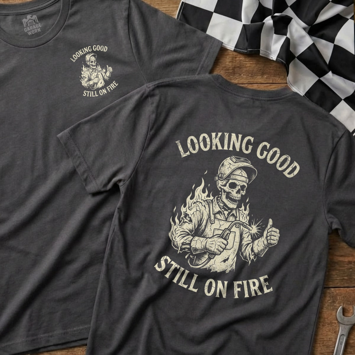 Skull wearing welding mask, giving thumbs up, with "Looking Good Still On Fire" text.