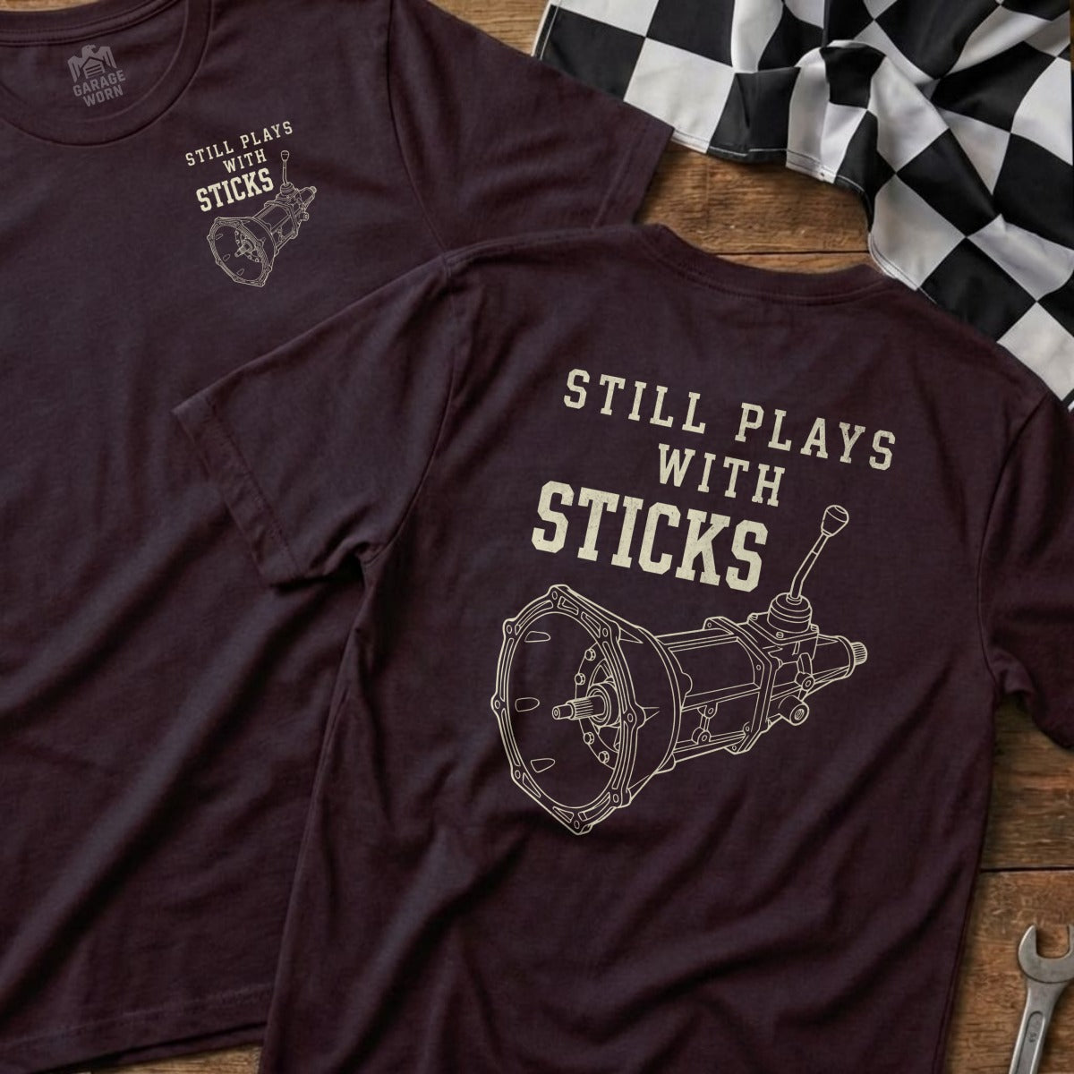 Maroon t-shirt with "Still Plays With Sticks" text and manual transmission graphic.