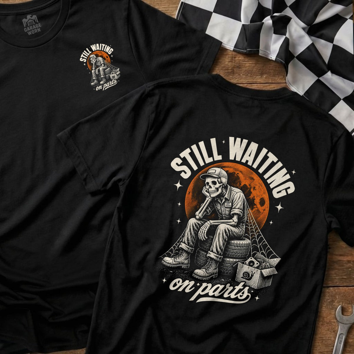 Black t-shirt with graphic of skeleton waiting on tires, text "Still Waiting on Parts".