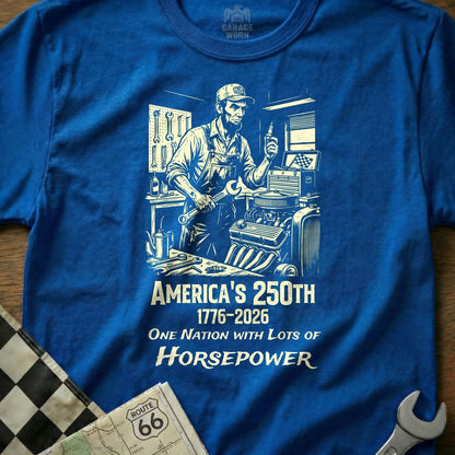 Blue t-shirt graphic with mechanic holding wrench and text "America's 250th One Nation with Lots of Horsepower".