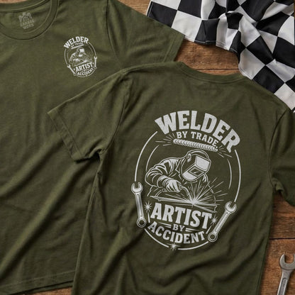Green t-shirt with "Welder By Trade, Artist By Accident" graphic.