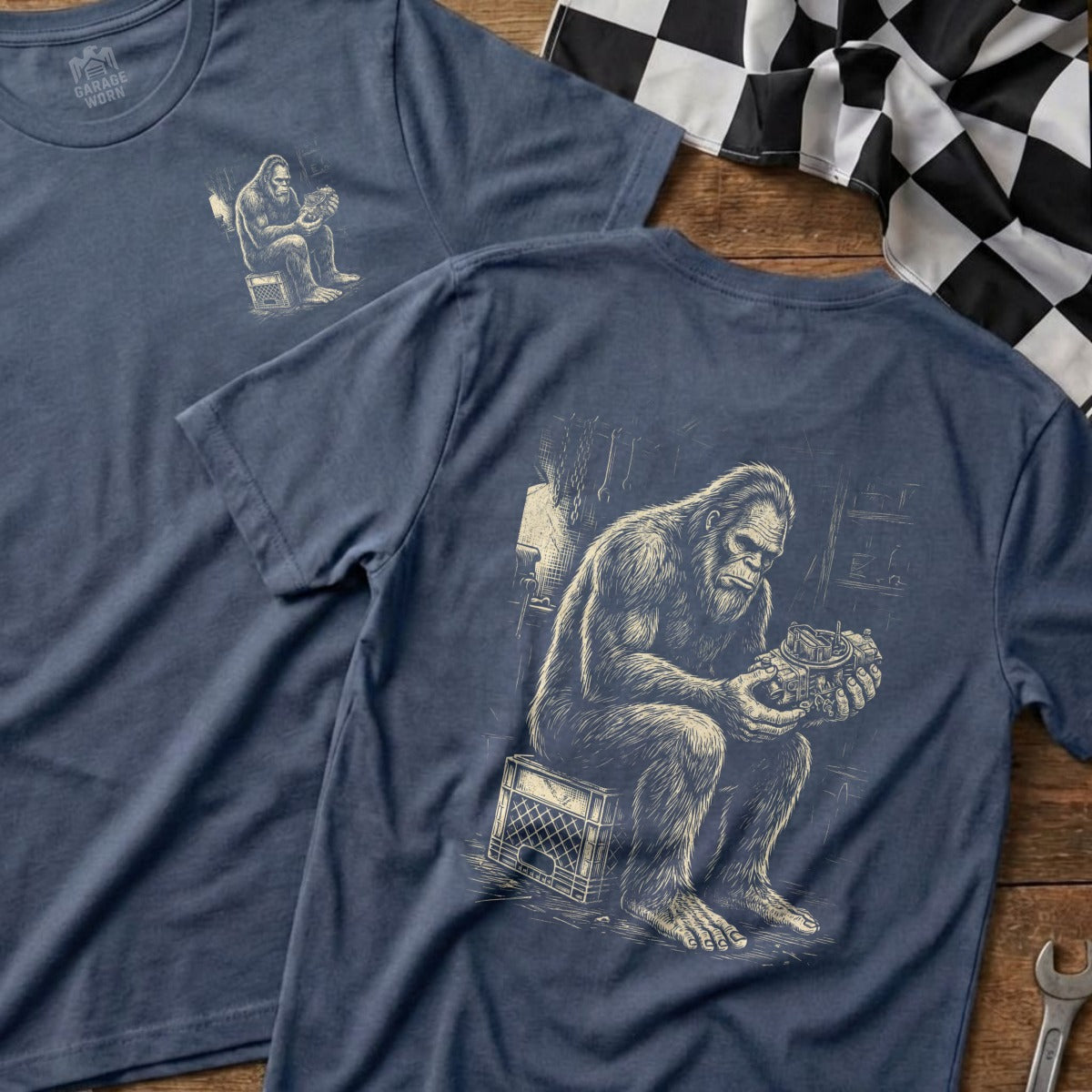 Two navy t-shirts, one with a Bigfoot graphic, the other showing a Bigfoot working on an engine.