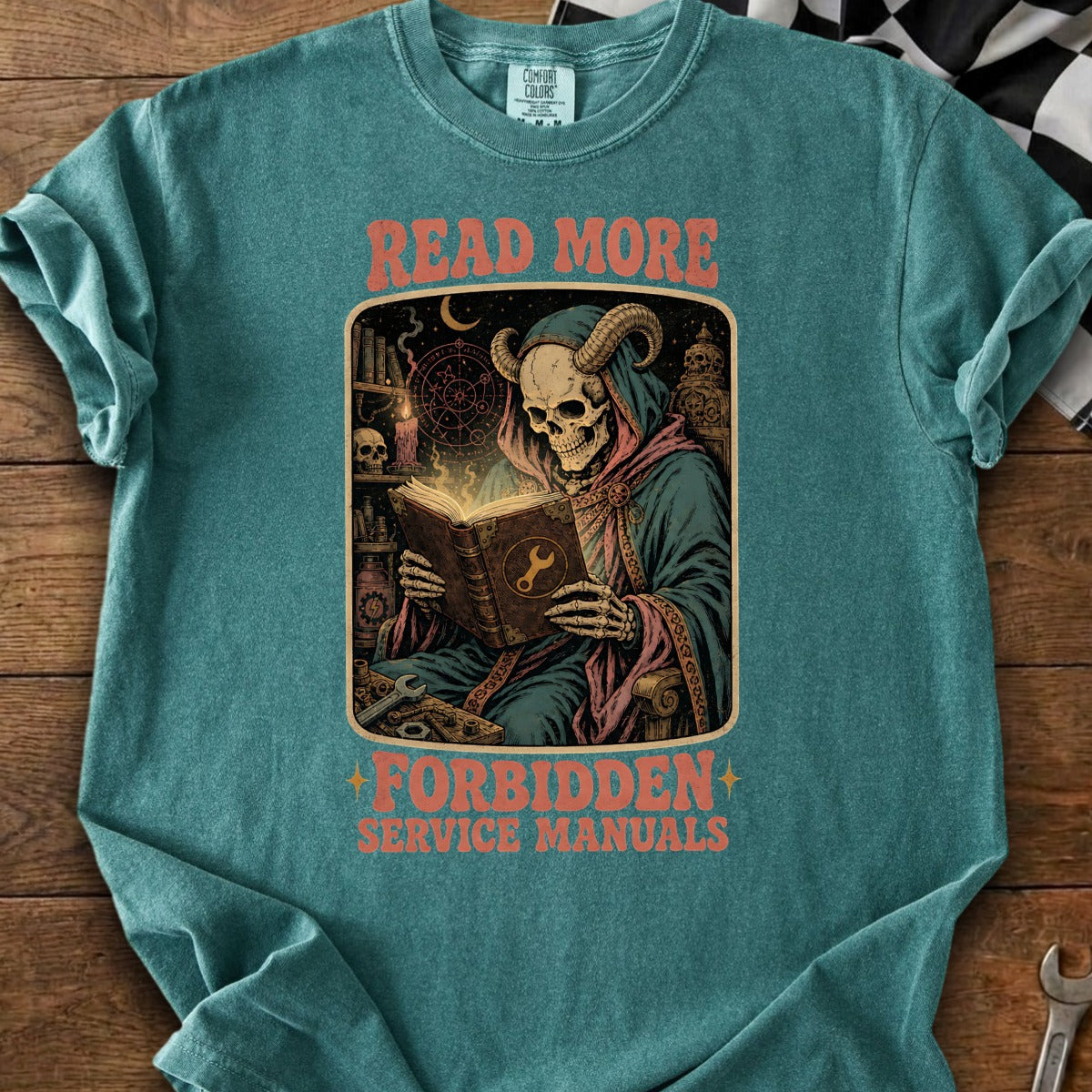 T-shirt graphic of a horned skeleton reading a book with "READ MORE FORBIDDEN SERVICE MANUALS" text.