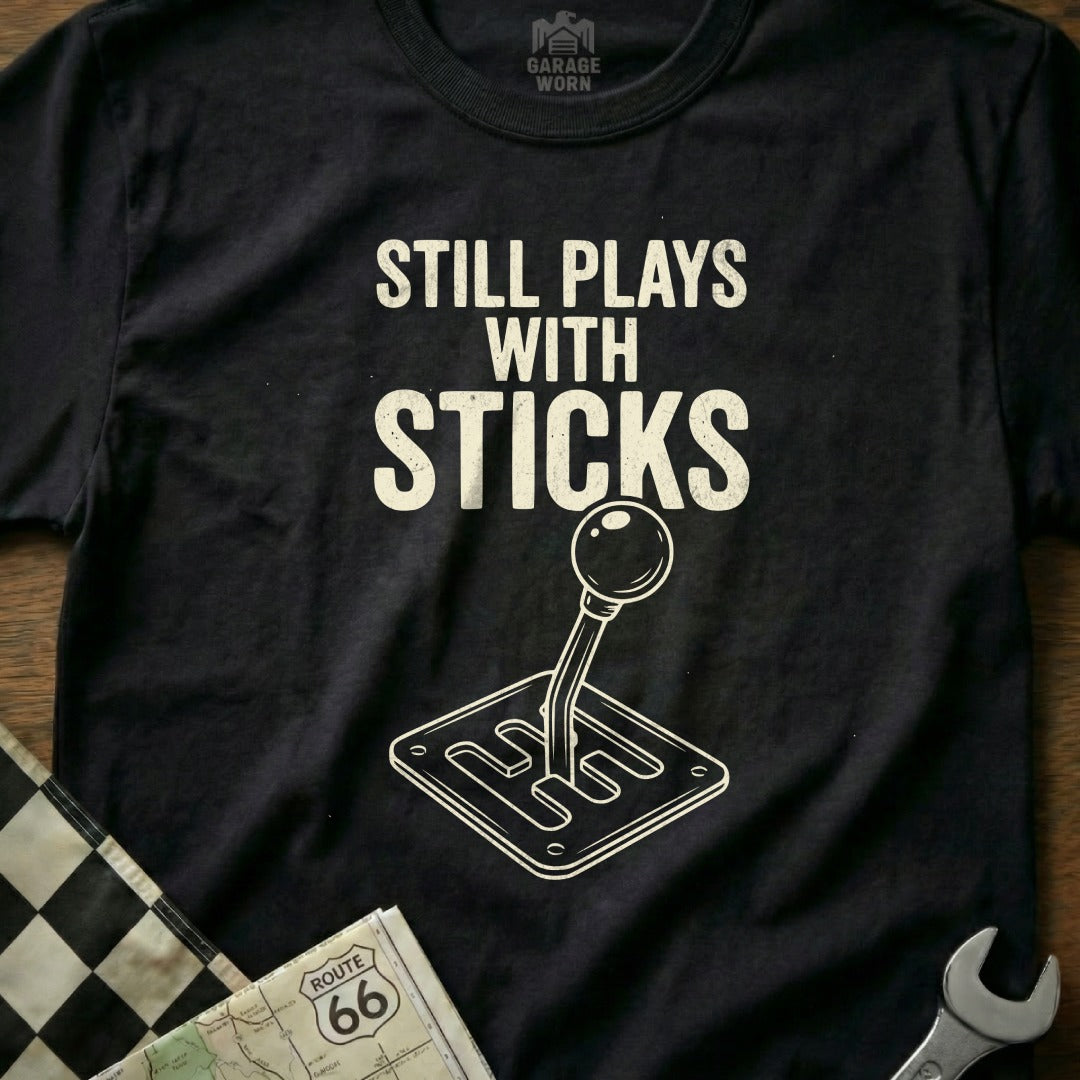 T-shirt with "Still Plays with Sticks" text and a manual transmission graphic.