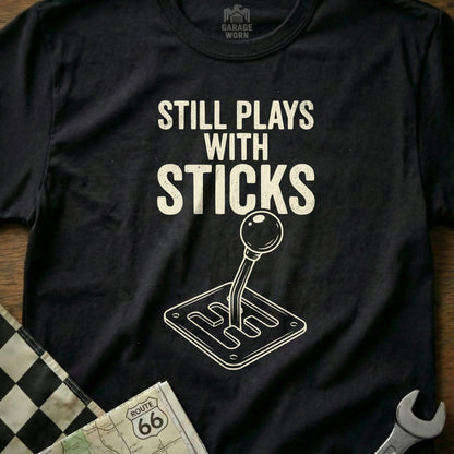 T-shirt with "Still Plays with Sticks" text and a manual transmission graphic.