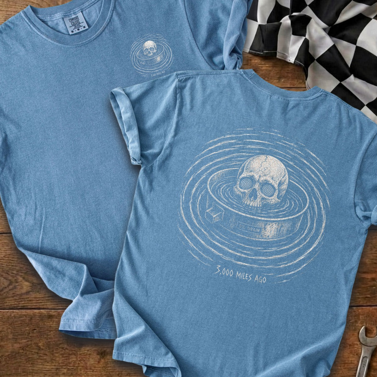 Blue t-shirt with a skull in a drain graphic and text "3,000 MILES AGO".