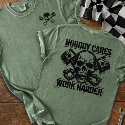 Green t-shirt with skull, pistons, and text "Nobody Cares Work Harder".
