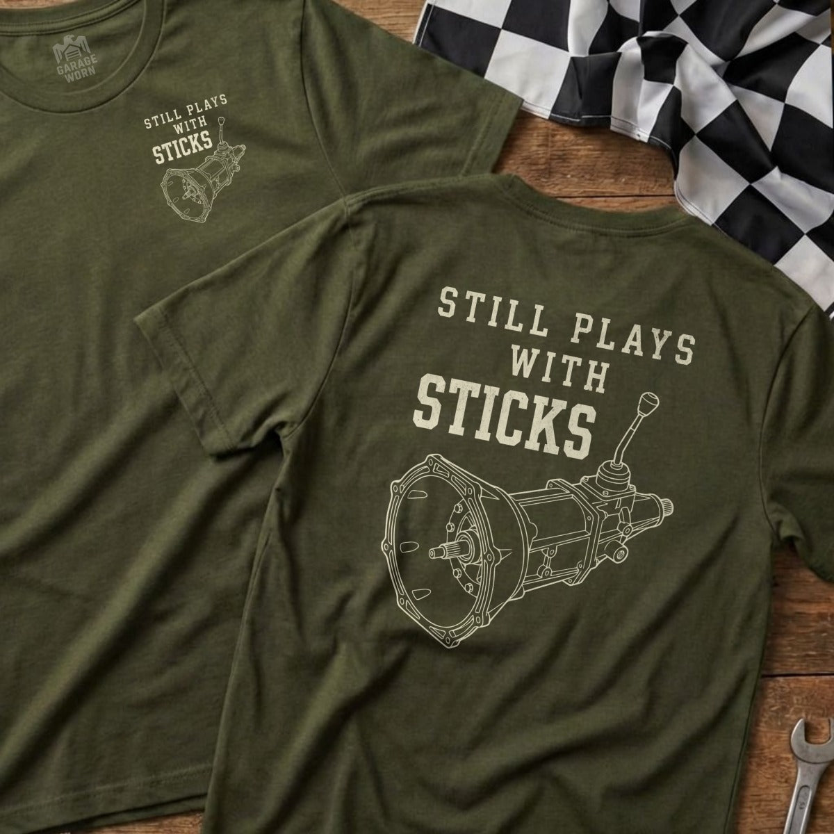 Two olive green t-shirts showing a manual transmission graphic and "STILL PLAYS WITH STICKS".