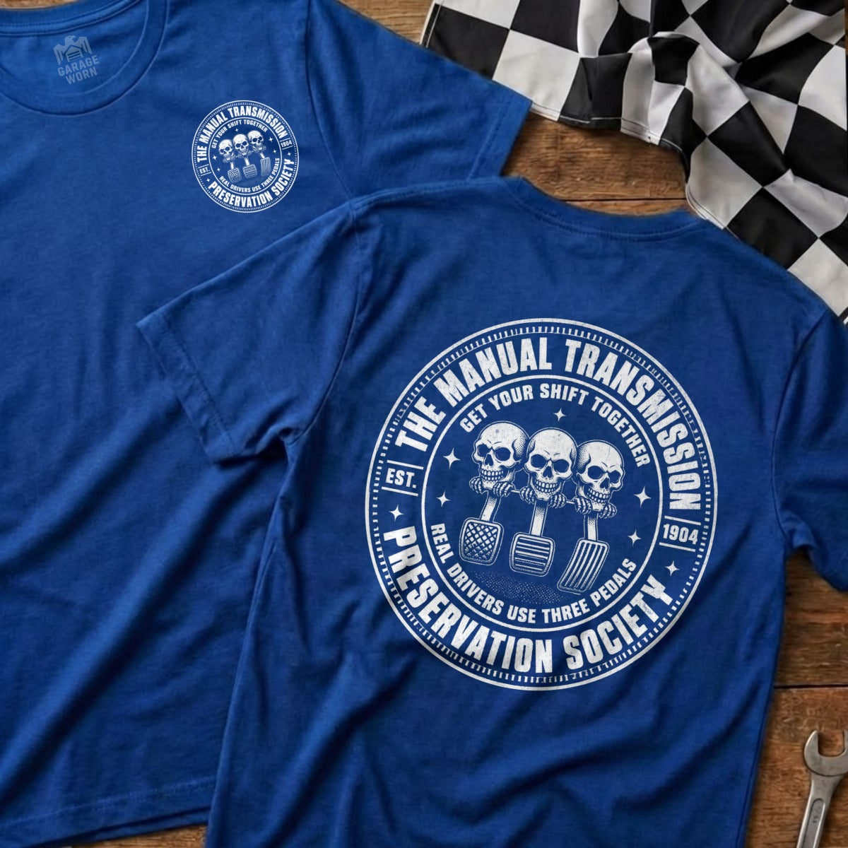 Blue t-shirt with white "Manual Transmission Preservation Society" graphic featuring skulls and pedals.