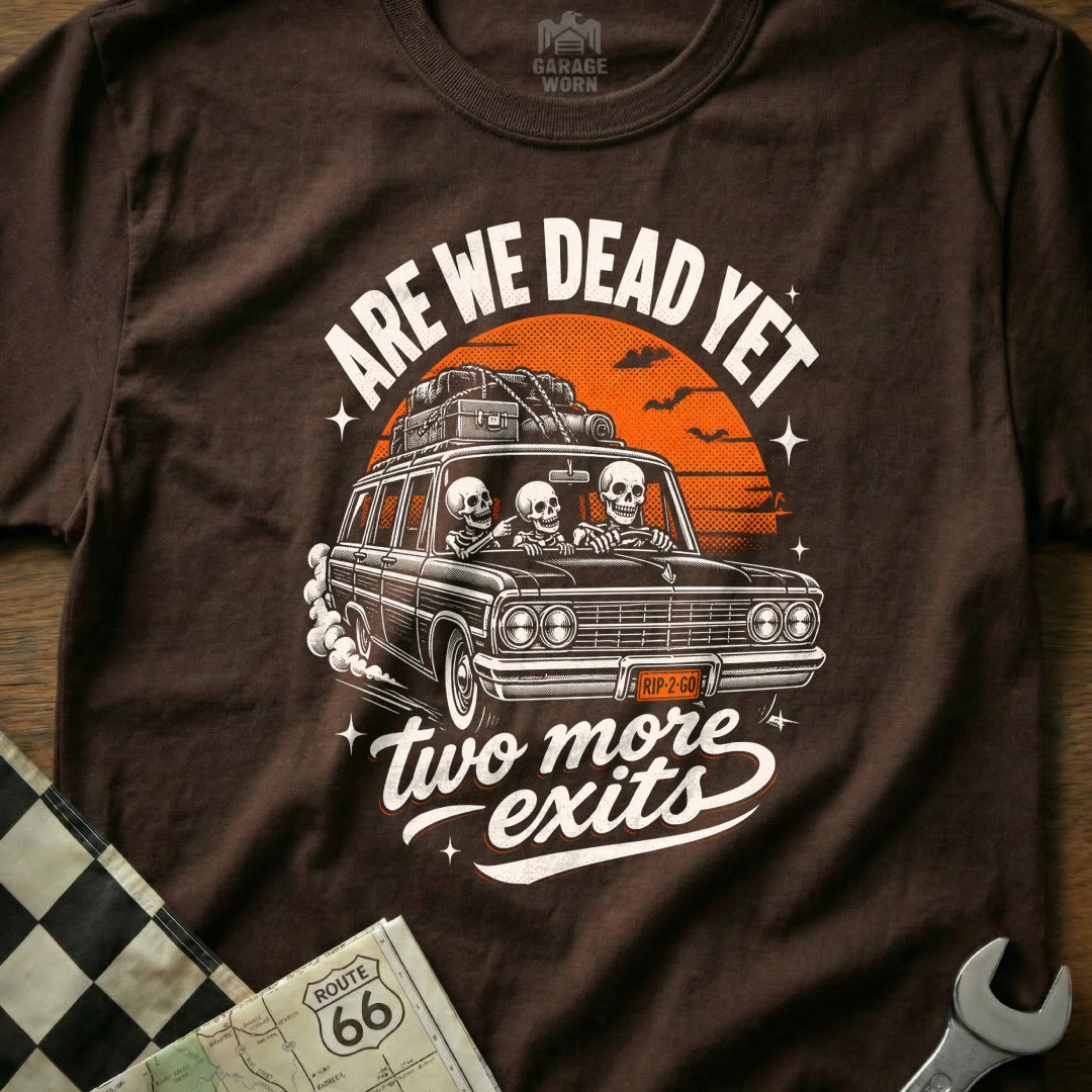 Skeletons drive a car with luggage, text "ARE WE DEAD YET" and "two more exits".