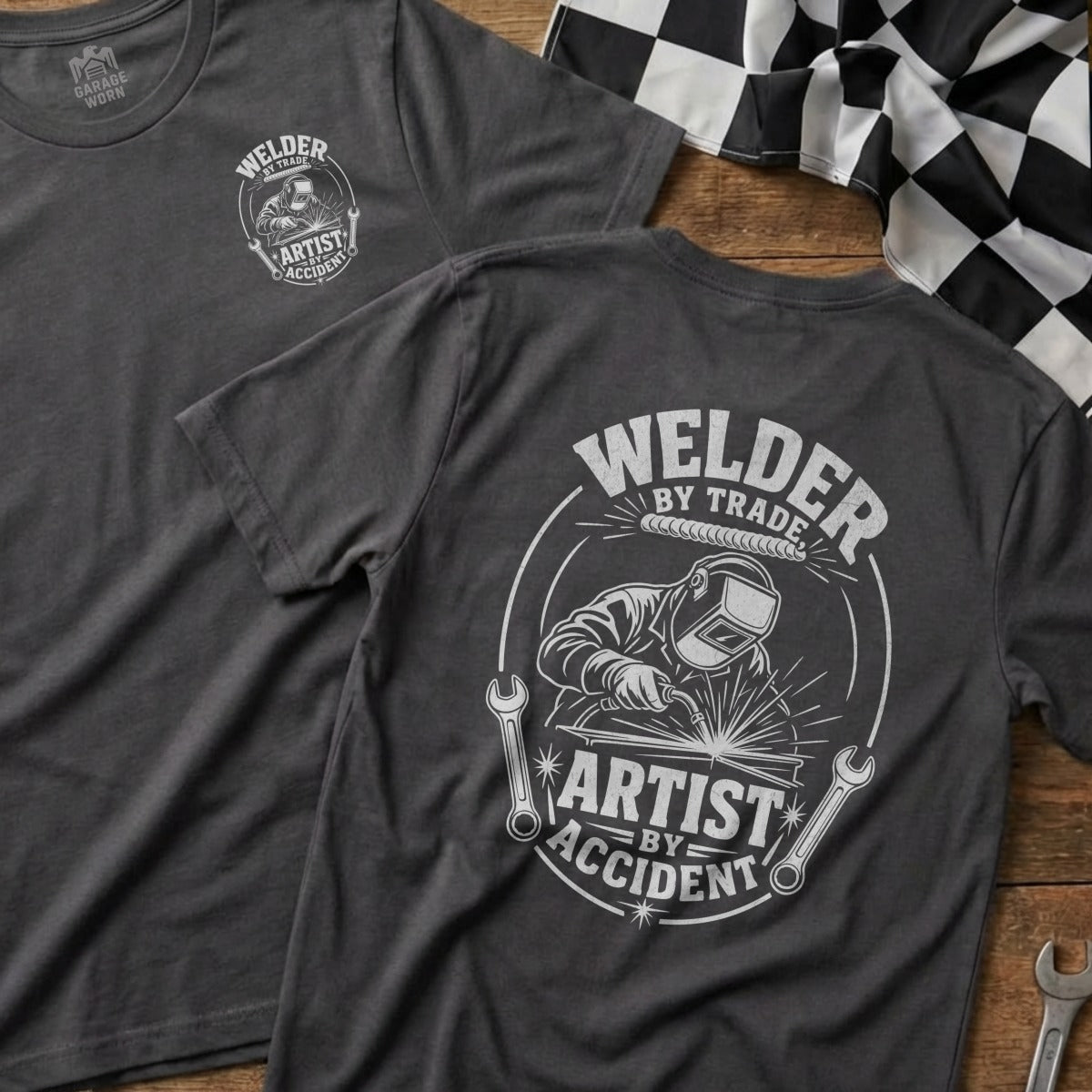 Dark gray t-shirt featuring a welder graphic with text "Welder by Trade, Artist by Accident".