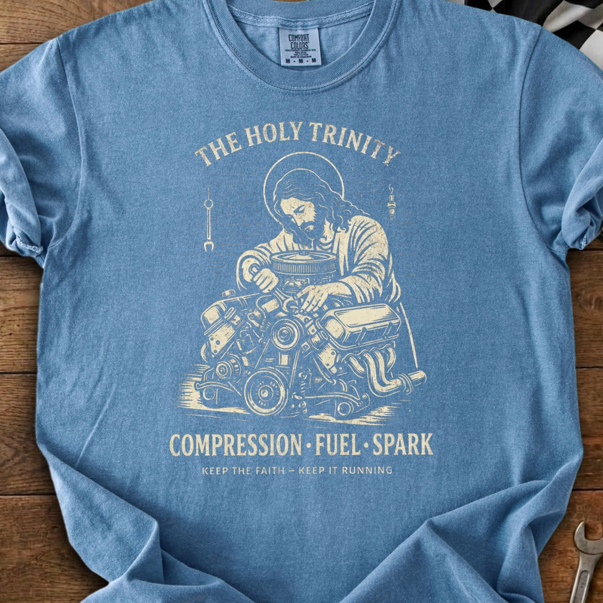Blue t-shirt with Jesus working on an engine, "The Holy Trinity" and "Compression Fuel Spark" text.
