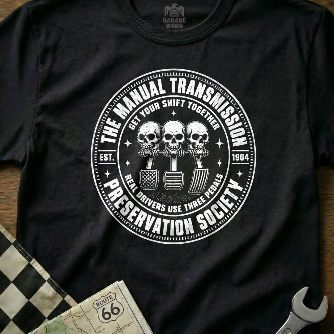 Black t-shirt with "Manual Transmission Preservation Society" circular graphic featuring skulls and pedals.