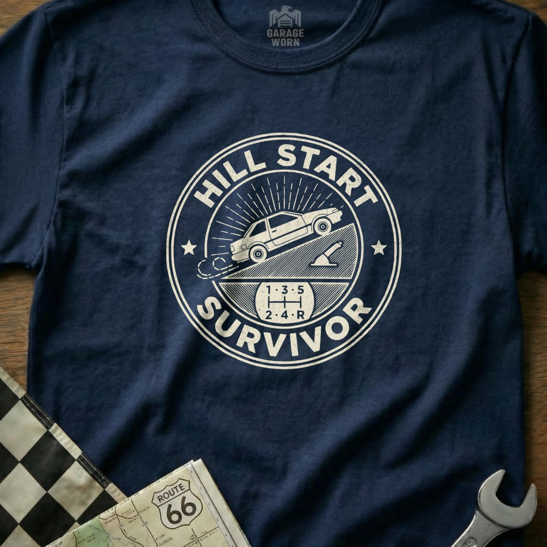 T-shirt graphic: "Hill Start Survivor" with manual car on incline.