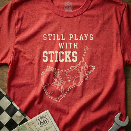 Red t-shirt with "Still Plays with Sticks" and a manual transmission diagram.