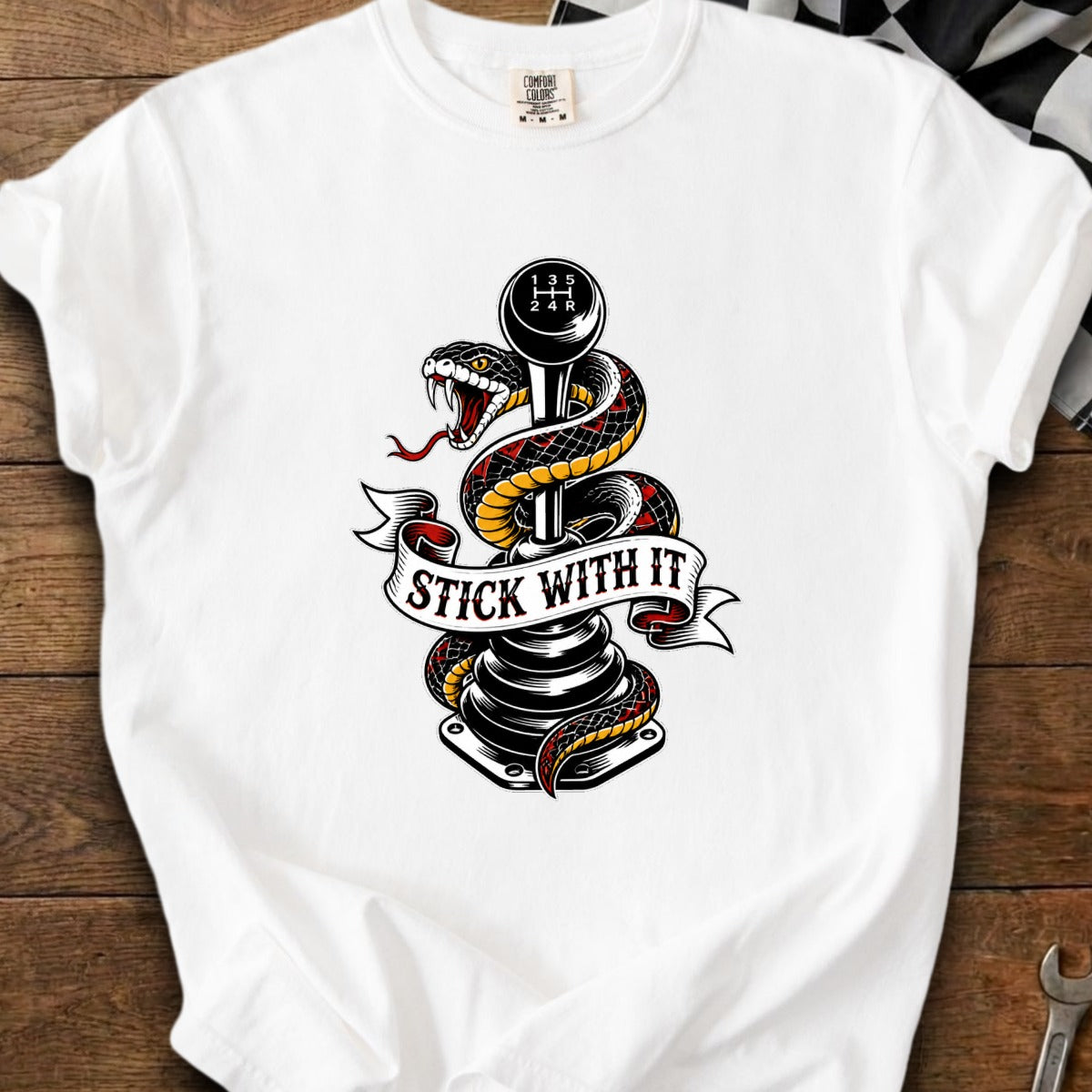 White t-shirt featuring a snake wrapped around a manual transmission shift knob with "STICK WITH IT" banner.