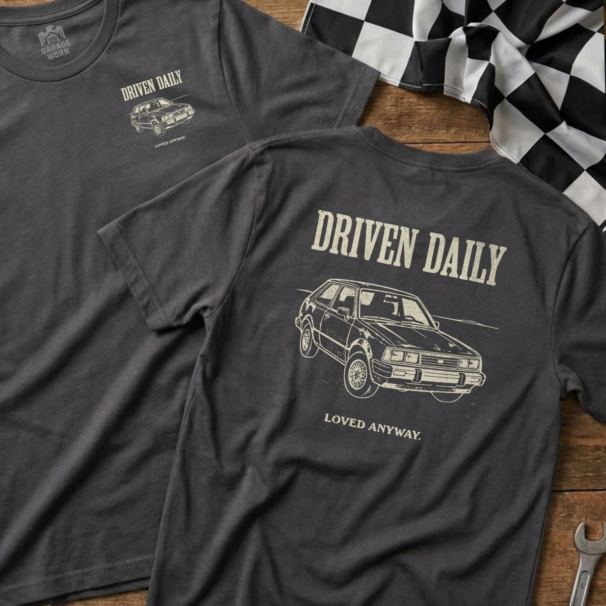 Dark grey t-shirt with "DRIVEN DAILY LOVED ANYWAY" and car graphic.