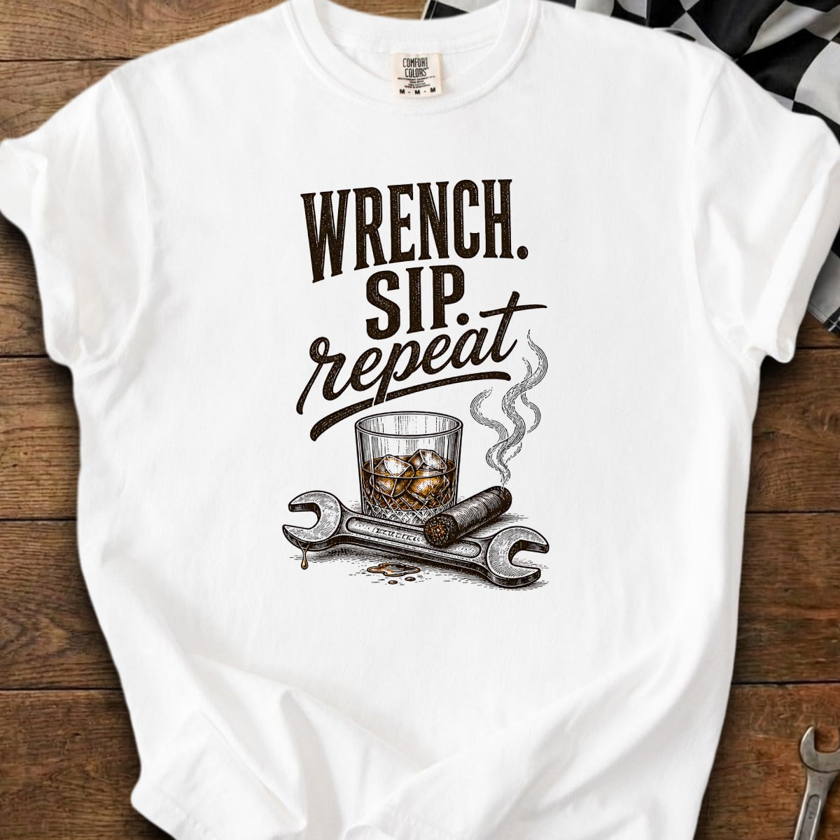 White t-shirt with text "WRENCH. SIP. repeat.", glass of whiskey, cigar, and wrenches.