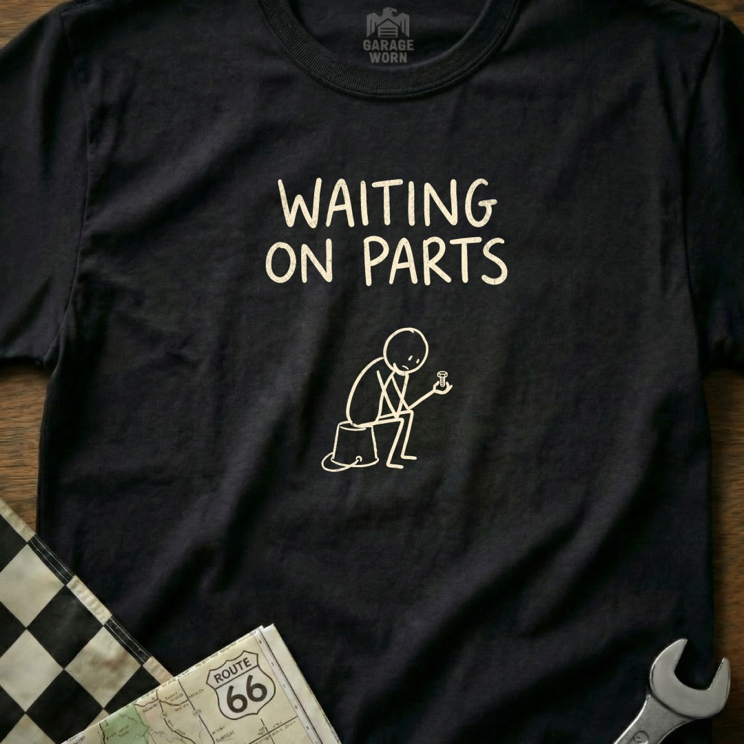 Black t-shirt with "WAITING ON PARTS" text and line drawing of a figure holding a bolt.