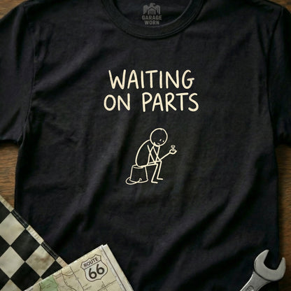 Black t-shirt with "WAITING ON PARTS" text and line drawing of a figure holding a bolt.