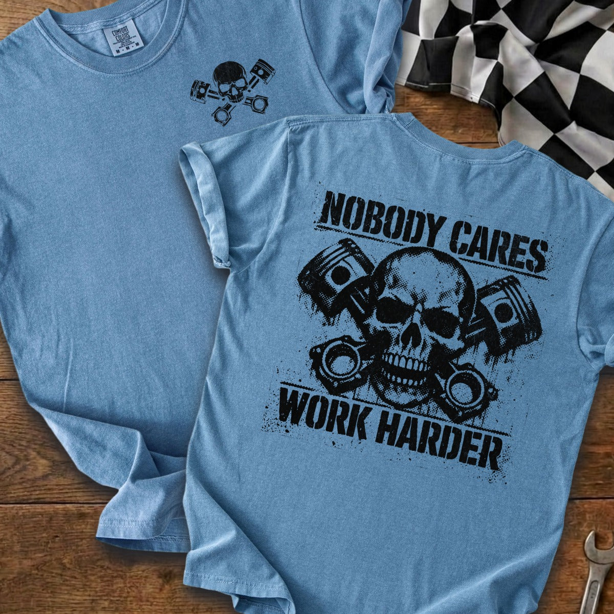 Blue t-shirt with black graphic of skull and pistons, text reads "Nobody Cares Work Harder".