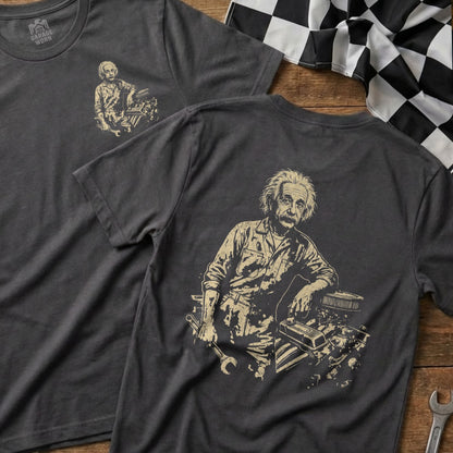 Albert Einstein in mechanic's overalls leaning on an engine, printed on a dark gray t-shirt.