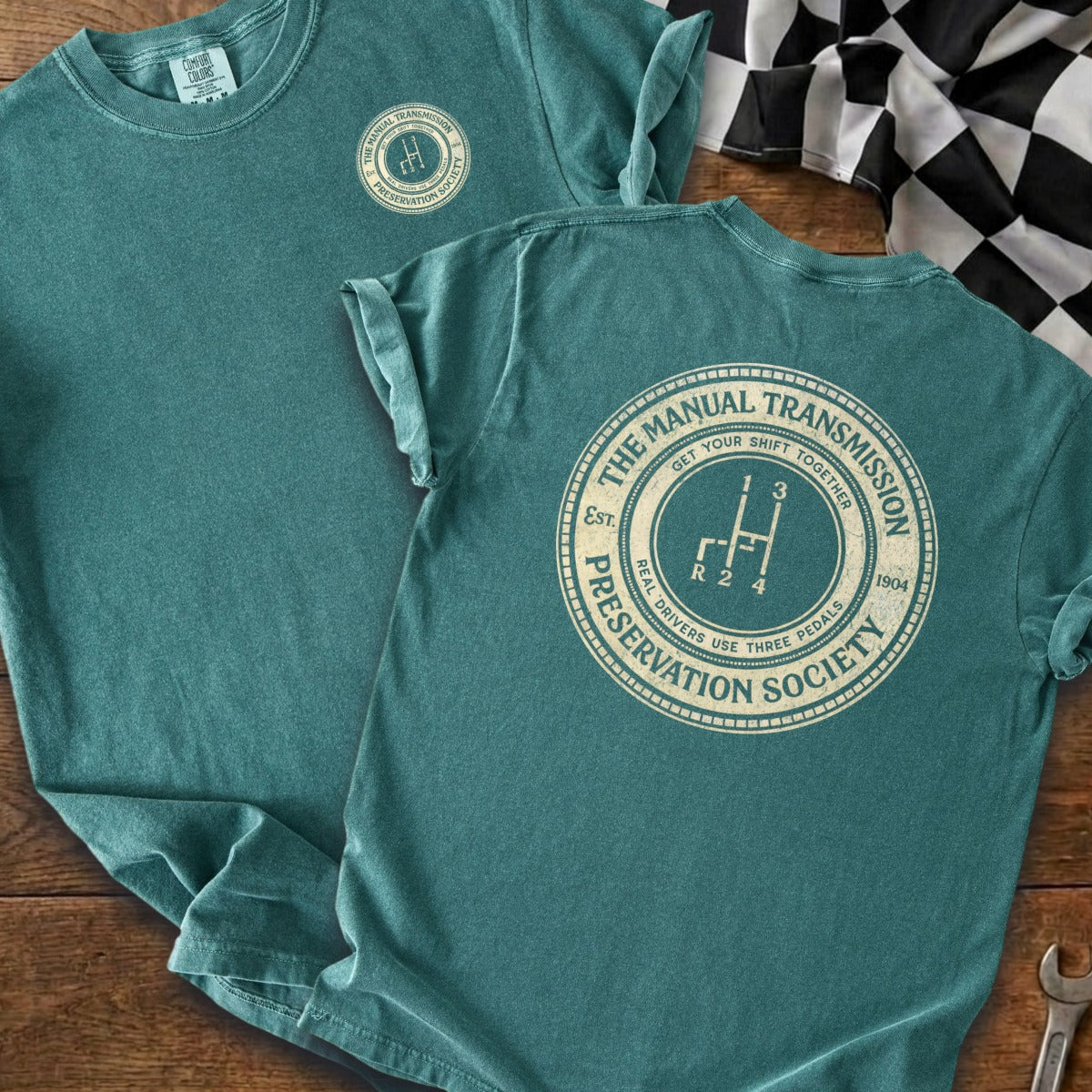 Teal t-shirt with circular graphic showing a gear shift and text about manual transmissions.