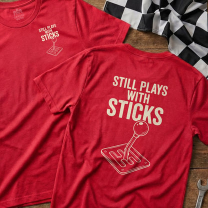 Two red t-shirts featuring "Still Plays With Sticks" and a manual gear shifter graphic.