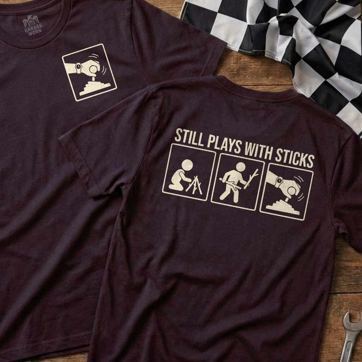 Maroon t-shirt with graphic of stick figures playing and text "STILL PLAYS WITH STICKS".