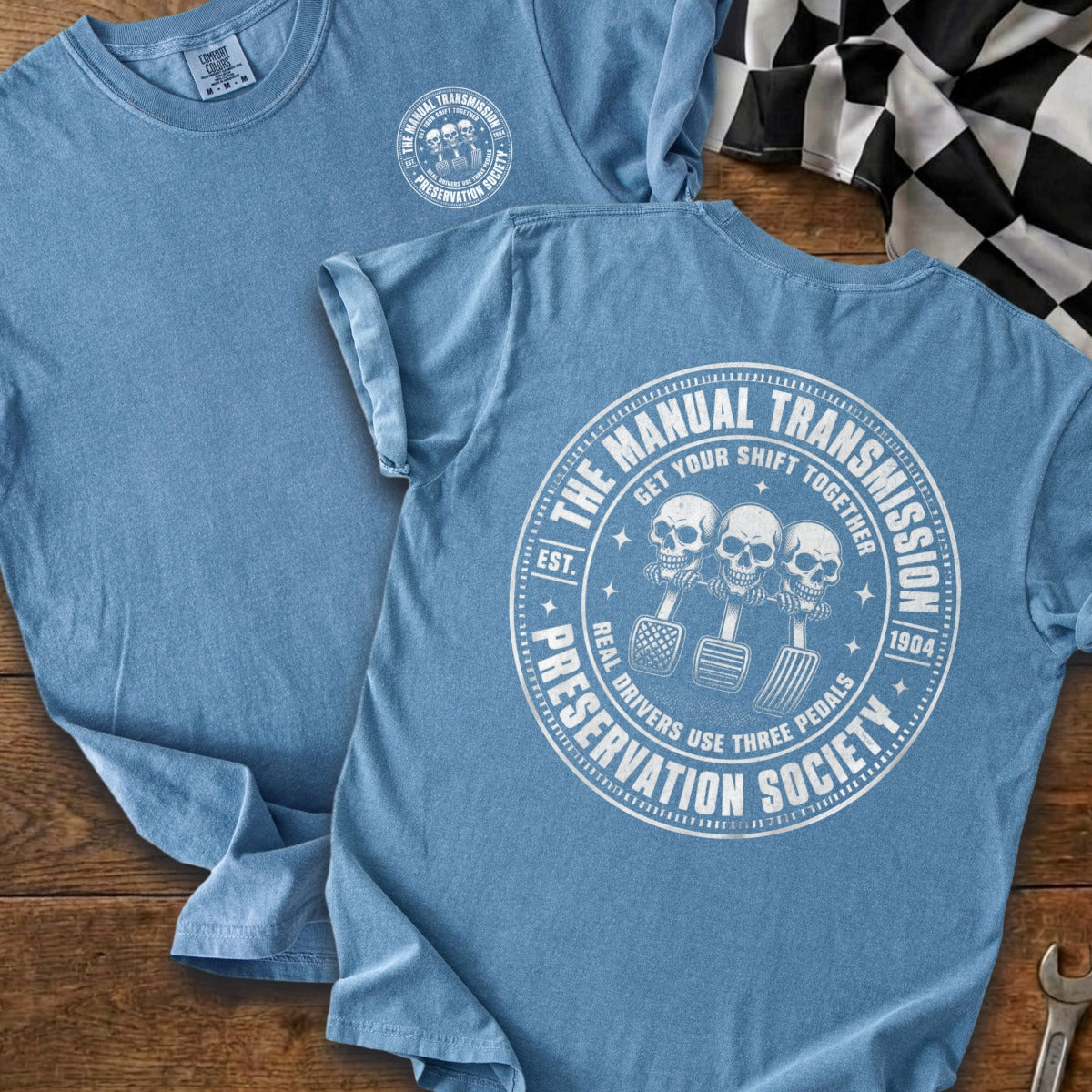 Blue t-shirt with "Manual Transmission Preservation Society" circular graphic of skulls and pedals.