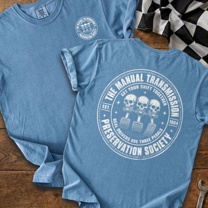 Blue t-shirt with "Manual Transmission Preservation Society" circular graphic of skulls and pedals.