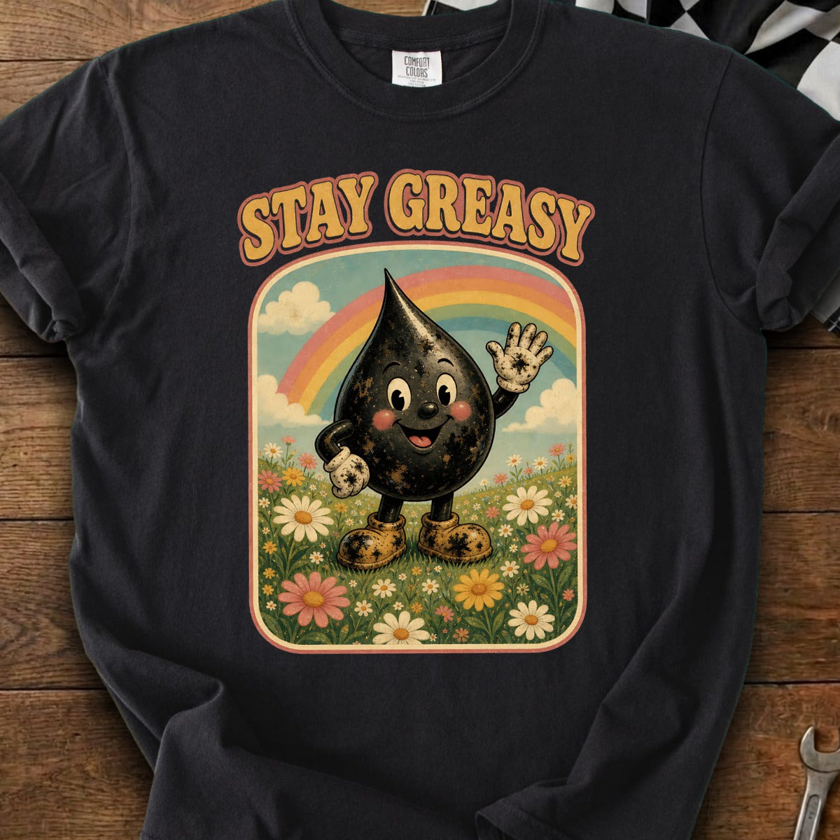Black oil drop character in a field of flowers with text "STAY GREASY" and rainbow.