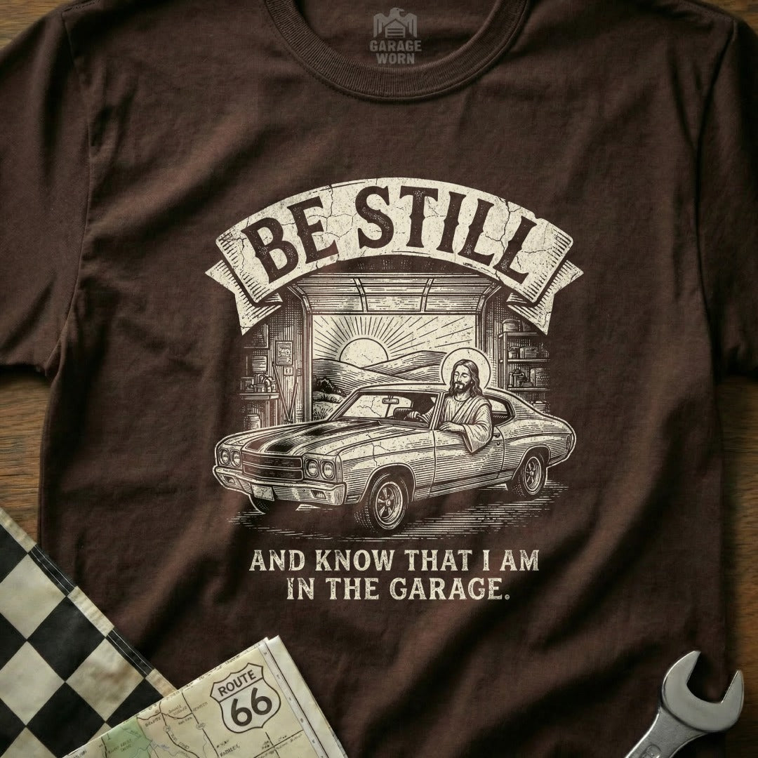 Brown t-shirt with Jesus driving a classic car and "Be Still and Know That I Am In The Garage" text.