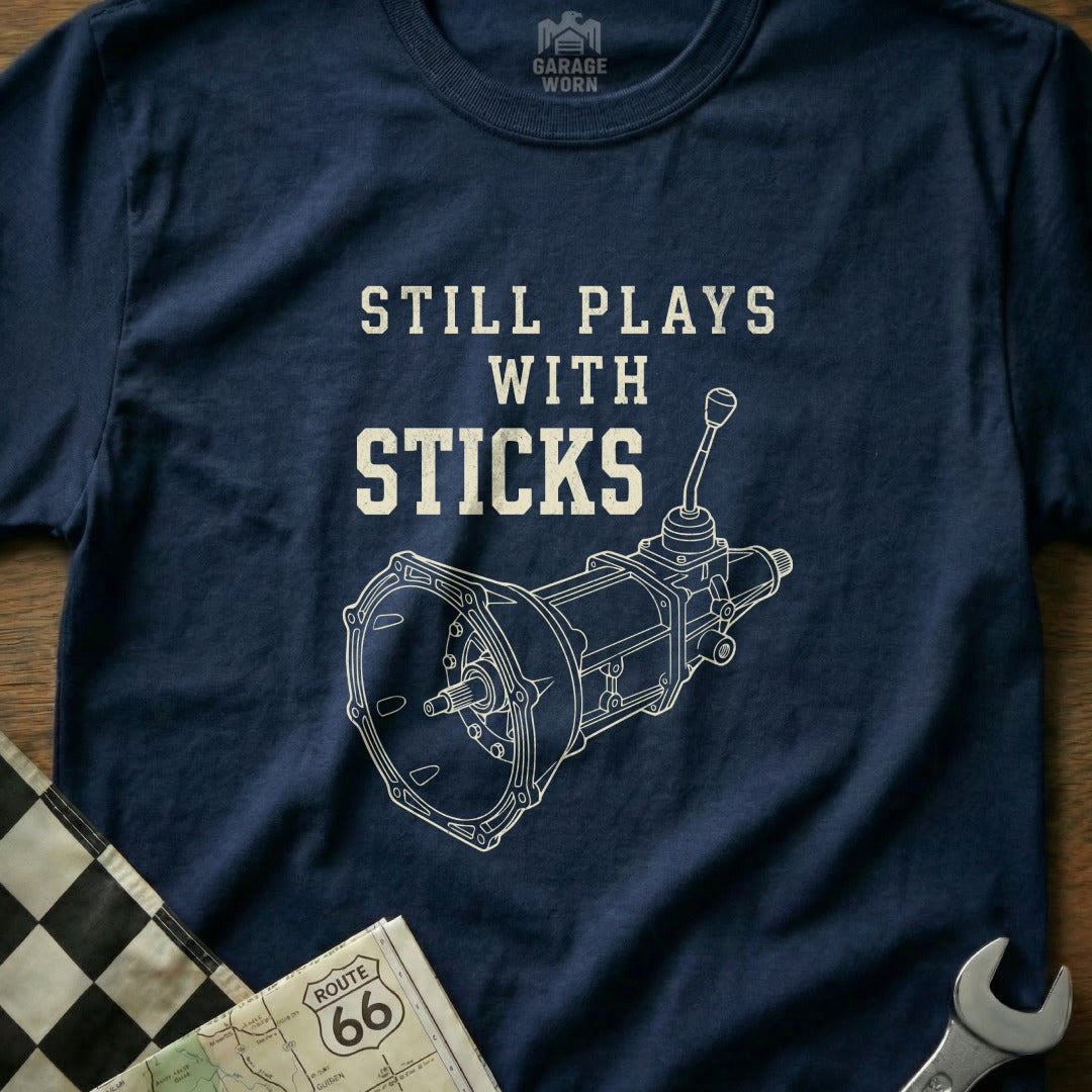 Navy t-shirt with "Still Plays With Sticks" and manual transmission diagram.