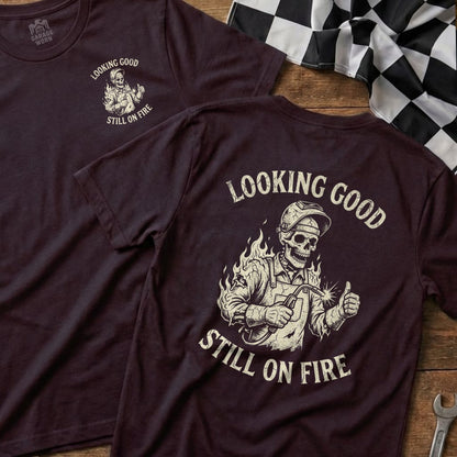 Burgundy t-shirt with a skeleton welder graphic and "Looking Good Still On Fire" text.