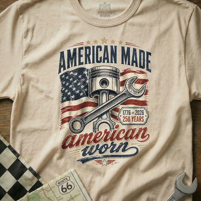Cream t-shirt with "American Made American Worn" text, piston, wrench, and US flag graphic.