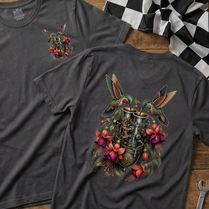 Two hummingbirds drink from a vintage carburetor surrounded by fuchsia flowers.