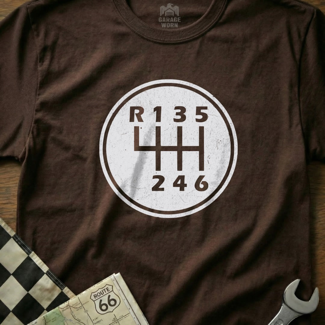 Brown t-shirt with a white circular graphic of a manual transmission gear shift pattern.