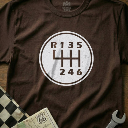 Brown t-shirt with a white circular graphic of a manual transmission gear shift pattern.