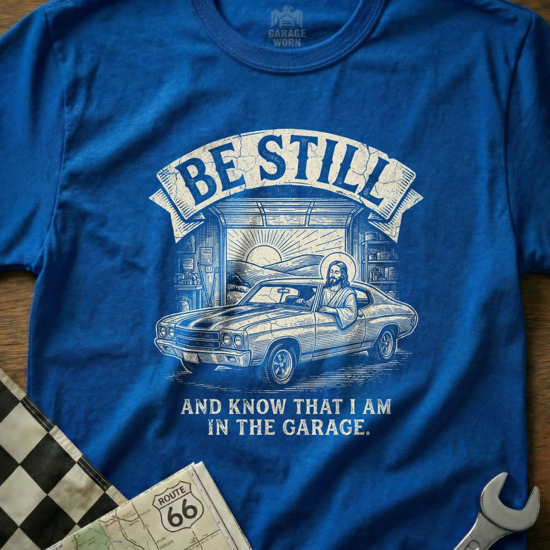 T-shirt with Jesus driving a classic car in a garage, reading "Be Still and Know That I Am In The Garage."