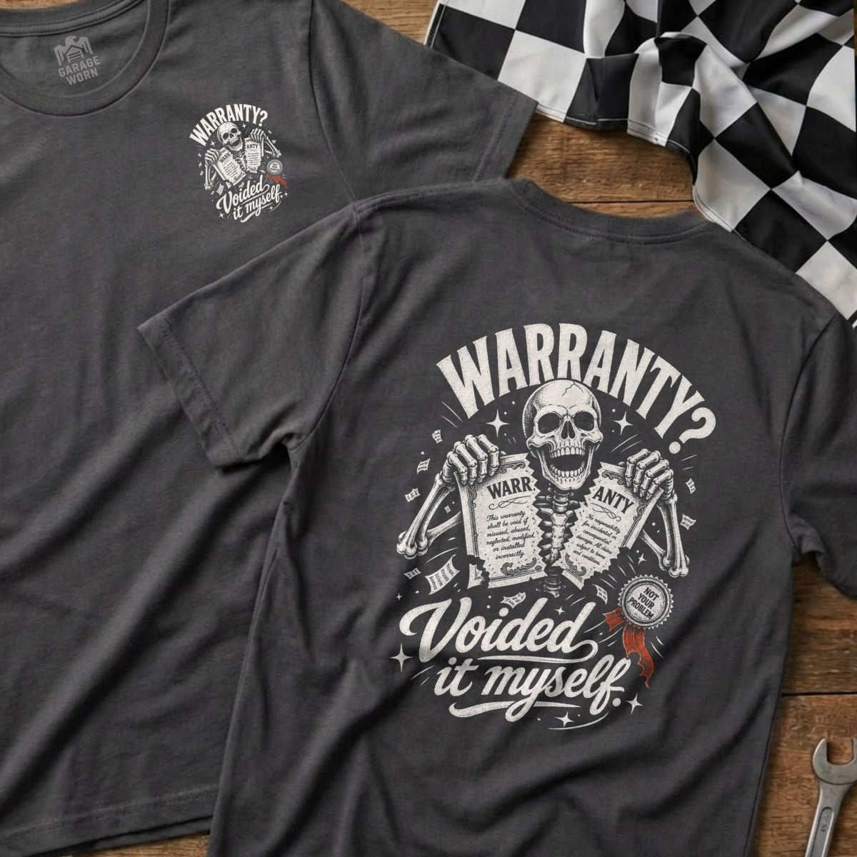 Dark grey t-shirt with skeleton graphic holding warranty papers, text reads "Warranty? Voided it myself."