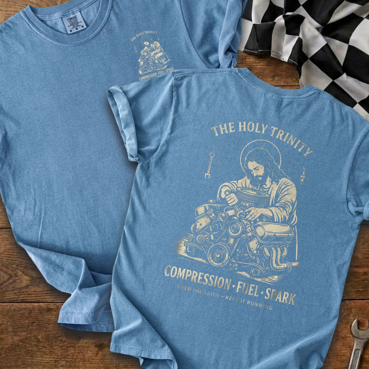 Blue t-shirt with graphic of Jesus working on an engine, text reads "The Holy Trinity Compression Fuel Spark".